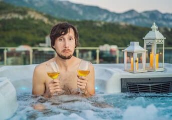 240_F_491908864_X9g7aVNwAvObs9IacFhf0oIXqsBLMF Man in hot tub holding two drinks.